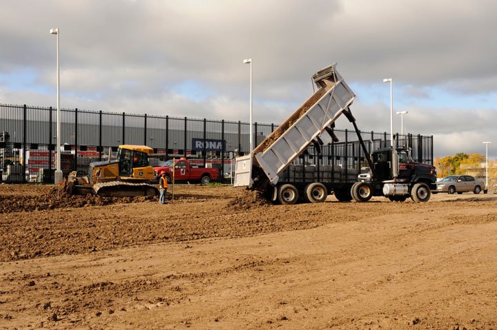 Triaxle dump truck leaving load on commerial site while dozer grades earth in background.