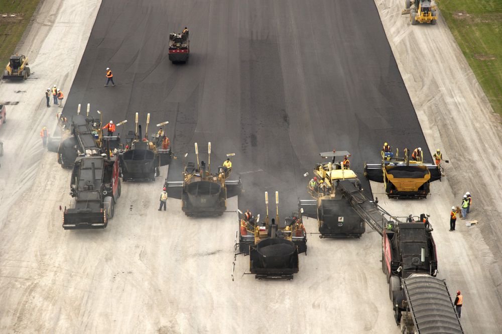 Aerial view of a six paver wide asphalt operation with two shuttle buggies supplying the pavers.