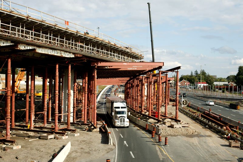 Traffic travelling through erected high load shoring system during the construction of a bridge.